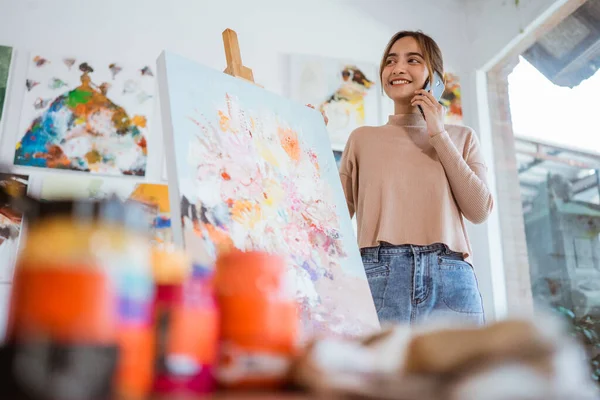 Upptagen målare står bredvid hennes målning när du ringer till hennes telefon — Stockfoto