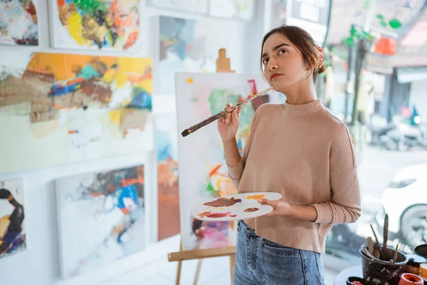 Vacker målare funderar på vad man ska måla medan hon sitter i sin verkstad — Stockfoto