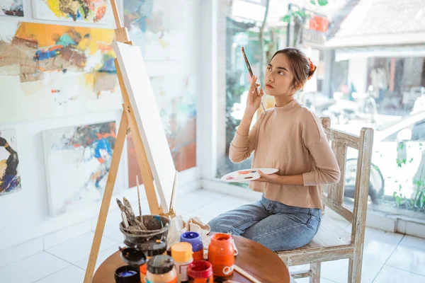 Vacker målare funderar på vad man ska måla medan hon sitter i sin verkstad — Stockfoto