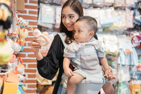Mãe pegar algum produto na loja do bebê enquanto carrega seu filho — Fotografia de Stock
