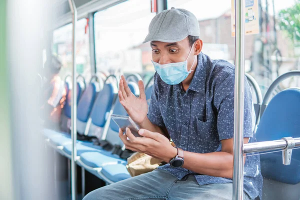 Feliz asiático homem aplaudindo celebrando olhando para smartphone enquanto em ônibus público com máscara — Fotografia de Stock