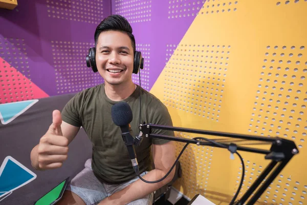 Smiling young man showing thumb up while recording podcast — Stock Photo, Image