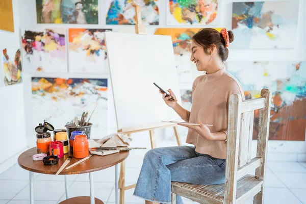 Female artist looking for inspiration from her mobile phone — Stock Photo, Image