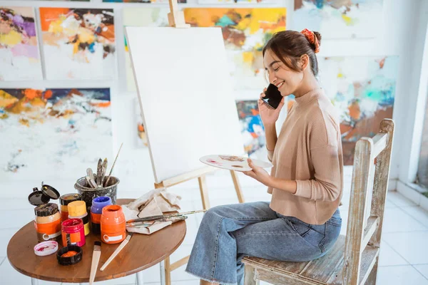 Жіночий художник малює на полотні, розмовляючи на своєму телефоні — стокове фото