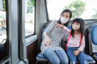 Asyalı anne kızını okula otobüsle giderken yüz maskesi takıyor.