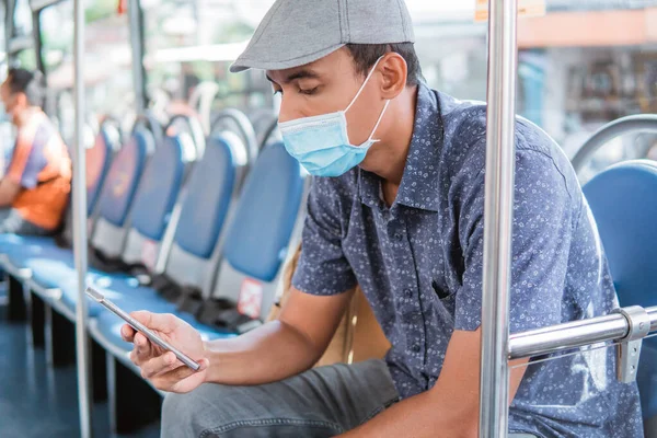 Masculino ásia usando telefone celular enquanto equitação público ônibus ou metro e desgaste máscara facial — Fotografia de Stock