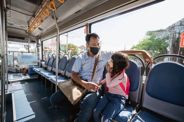 Азіатський батько везе свою дочку до школи, їздячи на автобусі громадського транспорту в масці для обличчя — стокове фото