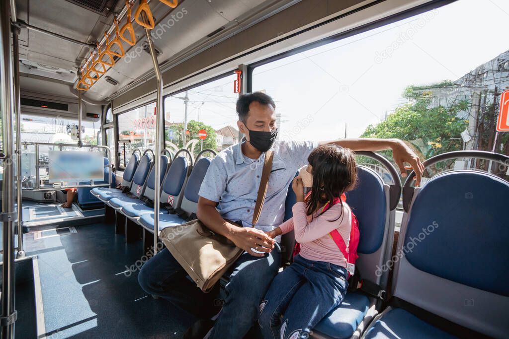 asian father taking his daughter to school by riding bus public transport wearing a face mask