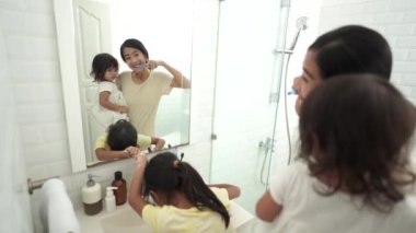 Mutlu Asyalı anne ve kız dişlerini birlikte fırçalıyorlar.