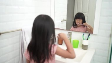 Asyalı küçük kız dişlerini yalnız banyoda fırçalar