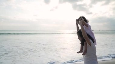 Anne sahilde kızını omuzlarında taşıyor.