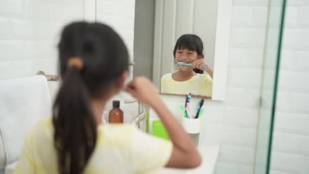 Asiática menina escova seus dentes sozinho no banheiro — Vídeo de Stock