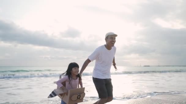 Azjatycki ojciec i córka działa na plaży grać z tekturowym samolotem zabawki — Wideo stockowe