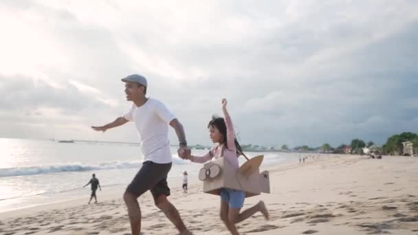 Asian father and daughter running at the beach play with cardboard toy airplane — Stock Video