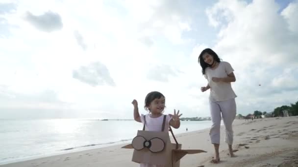Garoto correndo na praia brincar com avião de brinquedo de papelão com a mãe — Vídeo de Stock