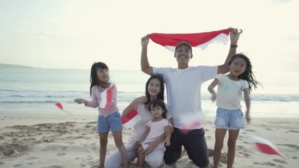 Vzrušený indonéský rodinný příznivec s indonéskou vlajkou na pláži společně — Stock video