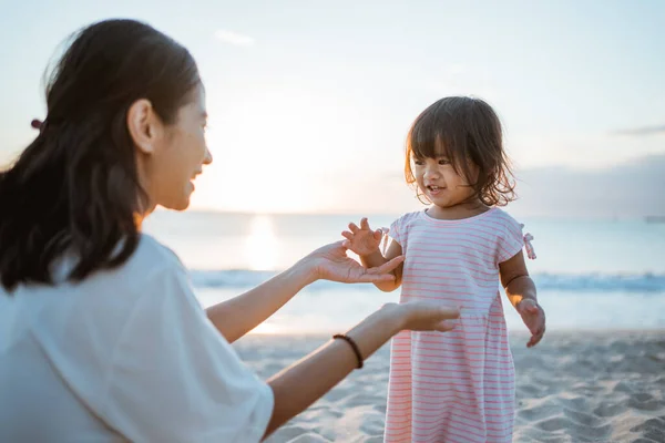 Gadis kecil gaun putih berdiri di pantai musim panas bermain dengan ibu — Stok Foto