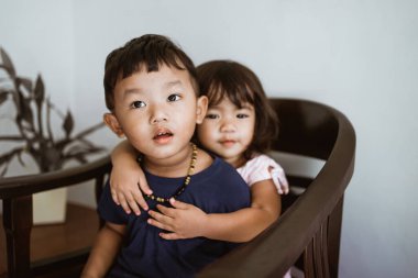 Sevgi dolu erkek ve kız kardeş bir sandalyede otururken sarılıyorlar.