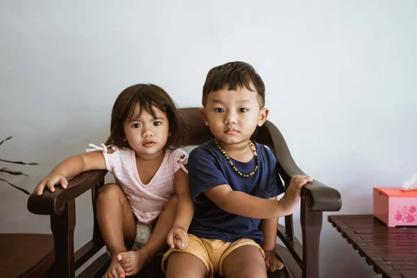 Hermano cariñoso y hermana pequeña abrazándose mientras se sienta en una silla —  Fotos de Stock