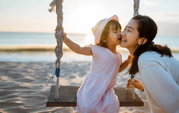 Dottern kysser sin mamma när hon svänger på stranden — Stockfoto