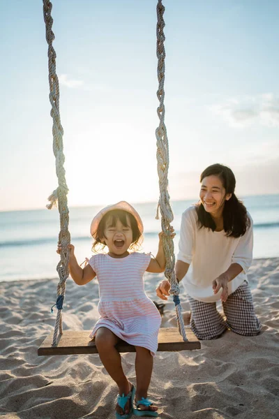 Glückliches kleines Mädchen und Mutter schaukeln am Strand — Stockfoto