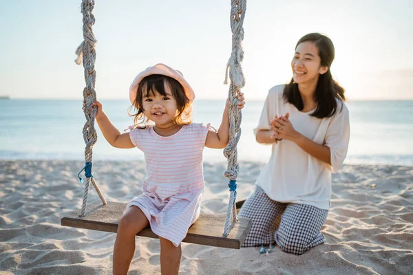 Glückliches kleines Mädchen und Mutter schaukeln am Strand — Stockfoto