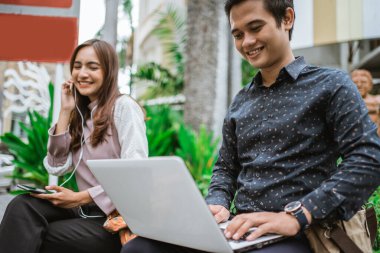 Adam bankta dizüstü bilgisayarla oturuyor.