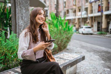 Zeki kadın parkta bankta oturmuş müzik dinliyor.