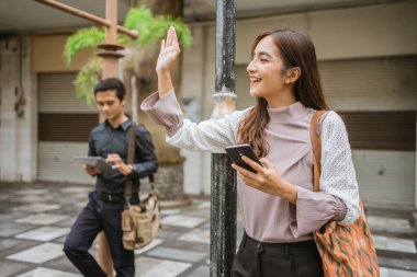 Asyalı kadın taksi beklerken elini sallıyor.