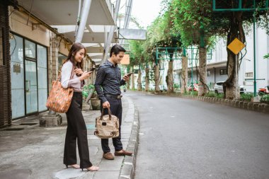 Adam ve kadın kaldırımda telefonlarını kullanarak gülümsüyor.