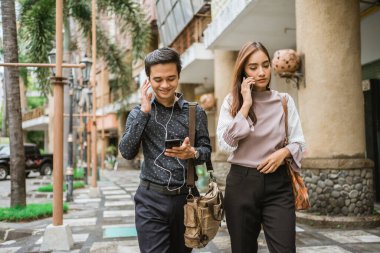 İş adamları kaldırımda yürüyor ve telefon kullanıyorlar.