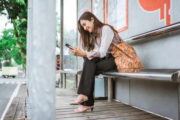 Geschäftsfrau auf einer Bushaltestelle, die auf den Bus wartet, während sie telefoniert — Stockfoto
