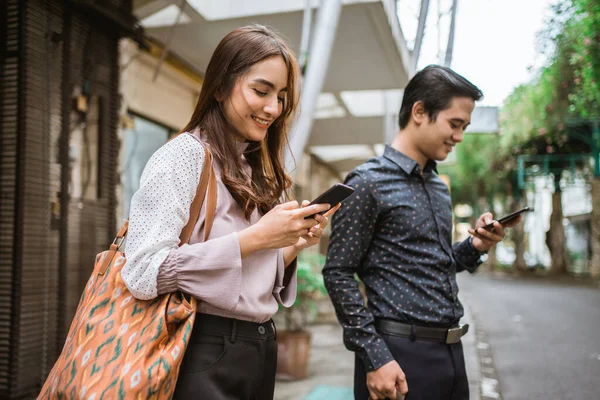 Mann und Frau stehen lächelnd auf dem Bürgersteig und benutzen ihr Handy — Stockfoto