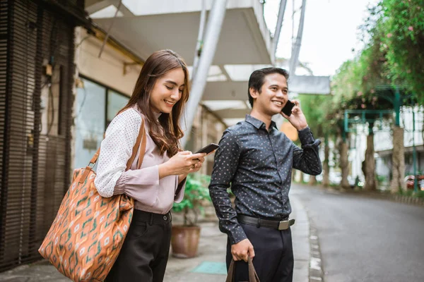 Mann und Frau stehen lächelnd auf dem Bürgersteig und benutzen ihr Handy — Stockfoto