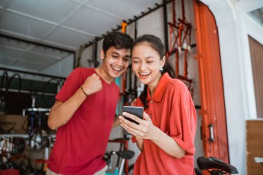 Bisiklet dükkanındaki heyecanlı Asyalı genç çiftler telefona bakarken şaşırdılar.