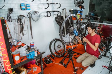 Kırmızı elbiseli genç adam aletlerle bisiklet kolu monte ediyor.