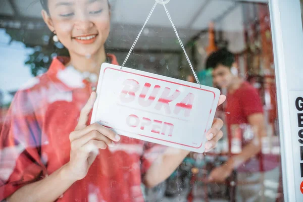 Uma menina vestindo uma camiseta vermelha com um sinal aberto na porta de vidro da frente — Fotografia de Stock