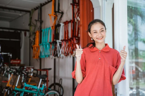 Una mujer con una camiseta de cuello rojo con los pulgares hacia arriba de pie delante de un puesto de bicicletas —  Fotos de Stock