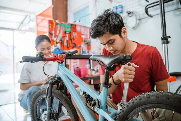 Joven mecánico montando una bicicleta nueva usando una llave inglesa en el taller — Foto de Stock