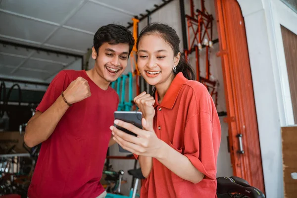 Vzrušené asijské mladé páry na kole shop překvapen při pohledu na telefon — Stock fotografie