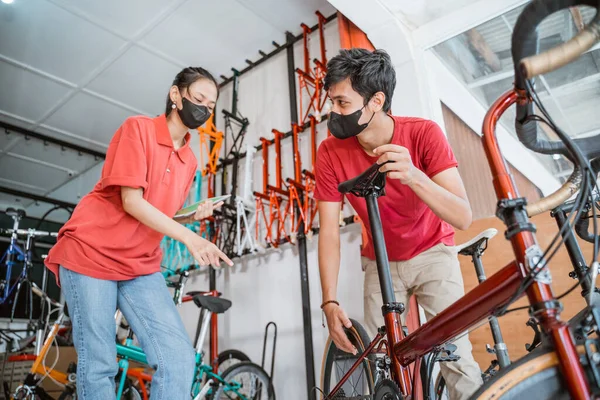 Un mecánico y una vendedora con máscara revisando la bicicleta nueva para el cliente —  Fotos de Stock