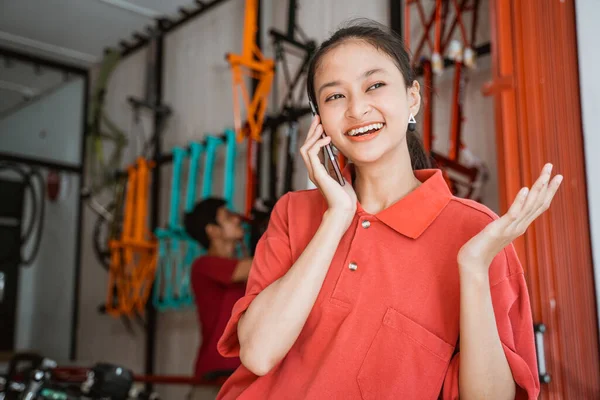 Mujer sonriendo felizmente mientras chatea usando un teléfono móvil en una tienda de bicicletas —  Fotos de Stock