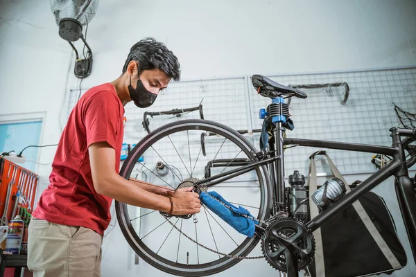 Un joven mecánico en la máscara de trabajo apriete el eje de la bicicleta —  Fotos de Stock
