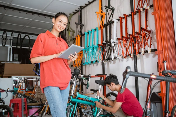 Kvinna ler mot kameran när du använder en digital tablett stående mot en cykelaffär — Stockfoto