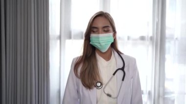 Tıbbi maske takan kadın doktor kameraya bakıyor.