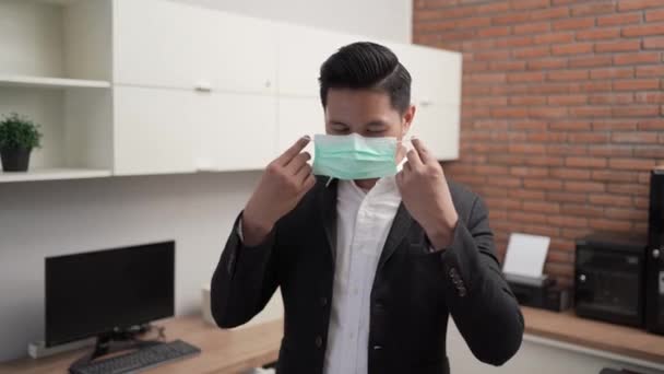 Hombre de negocios con una máscara facial mientras trabaja en su oficina — Vídeos de Stock