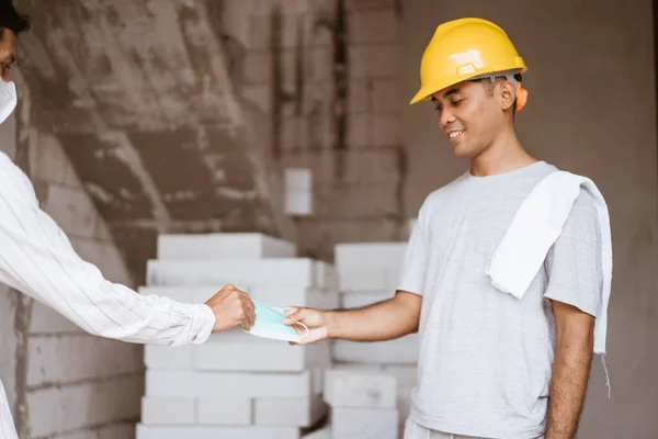 Bouwvakker krijgt een masker tijdens het werken aan een bouwproject — Stockfoto