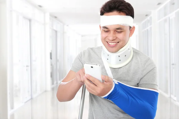 Skadet ung mann ser glad ut når han spiller smarttelefon – stockfoto