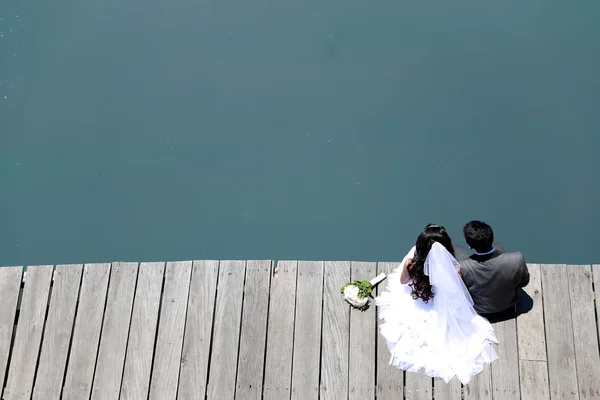 Bride and groom sitting on the edge of the river bridge — Stock Photo, Image