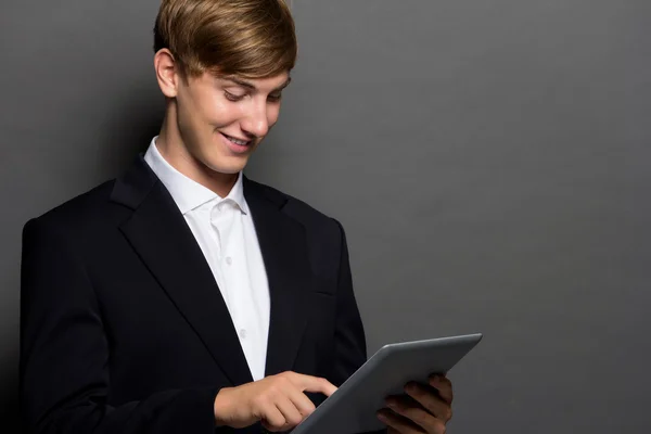 Mladý muž v černém obleku pomocí tablet, samostatný — Stock fotografie